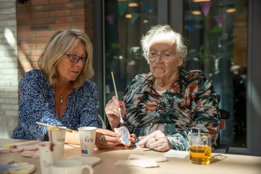 Oude vrouw en wat jongere vrouw schilderen samen keramiek aan tafel